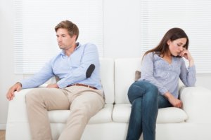 A couple sitting not looking at each other while sitting on a couch