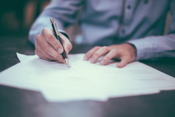 Close up of man's hands as he writes on paperwork with a pen